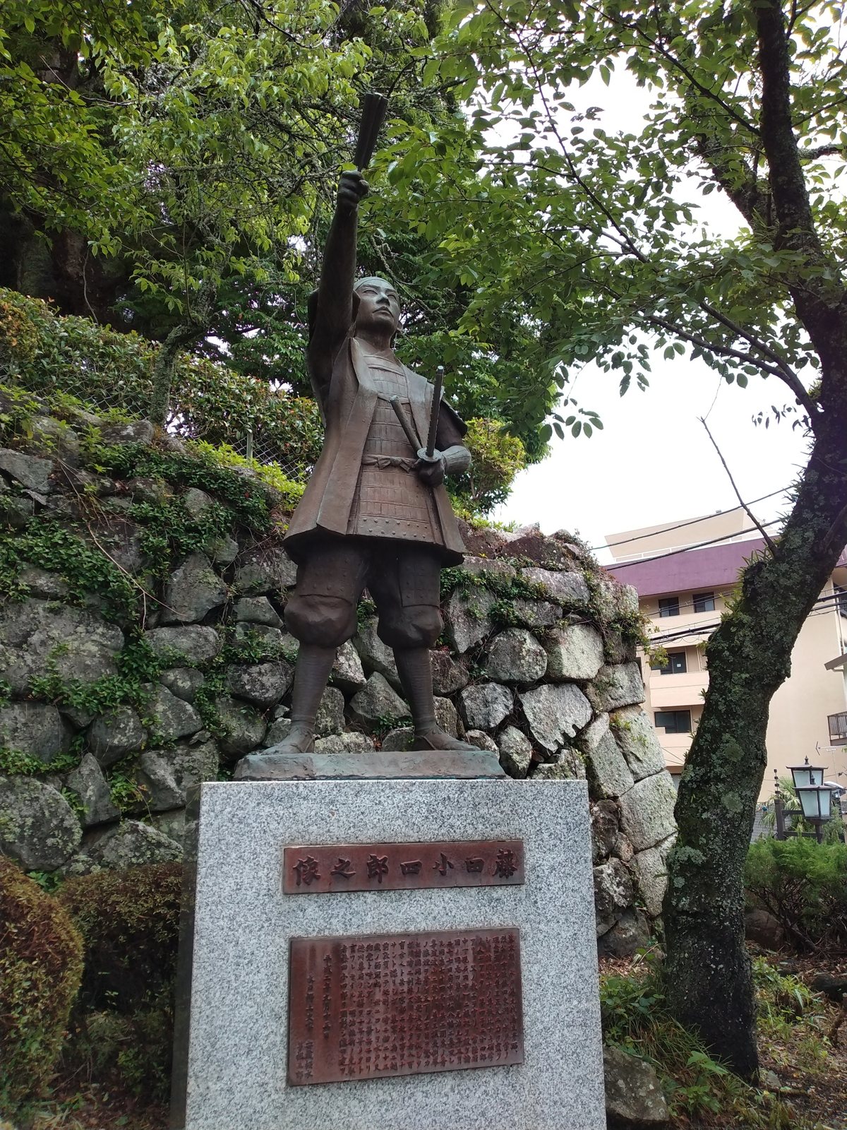 石垣を背に立つ藤田小四郎の像。右腕を高く上げ、左手には刀を提げている