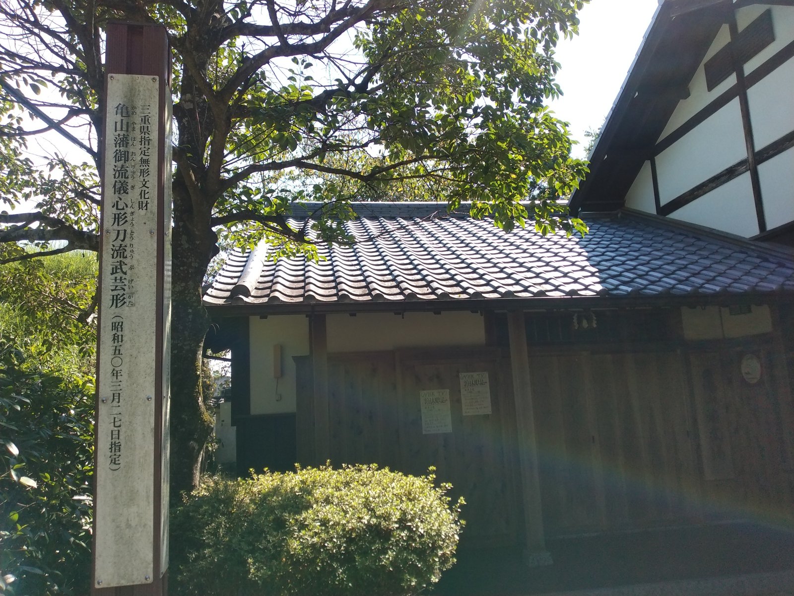 「亀山藩御流儀 心形刀流武芸形」の標柱と、亀山演武場の建物
