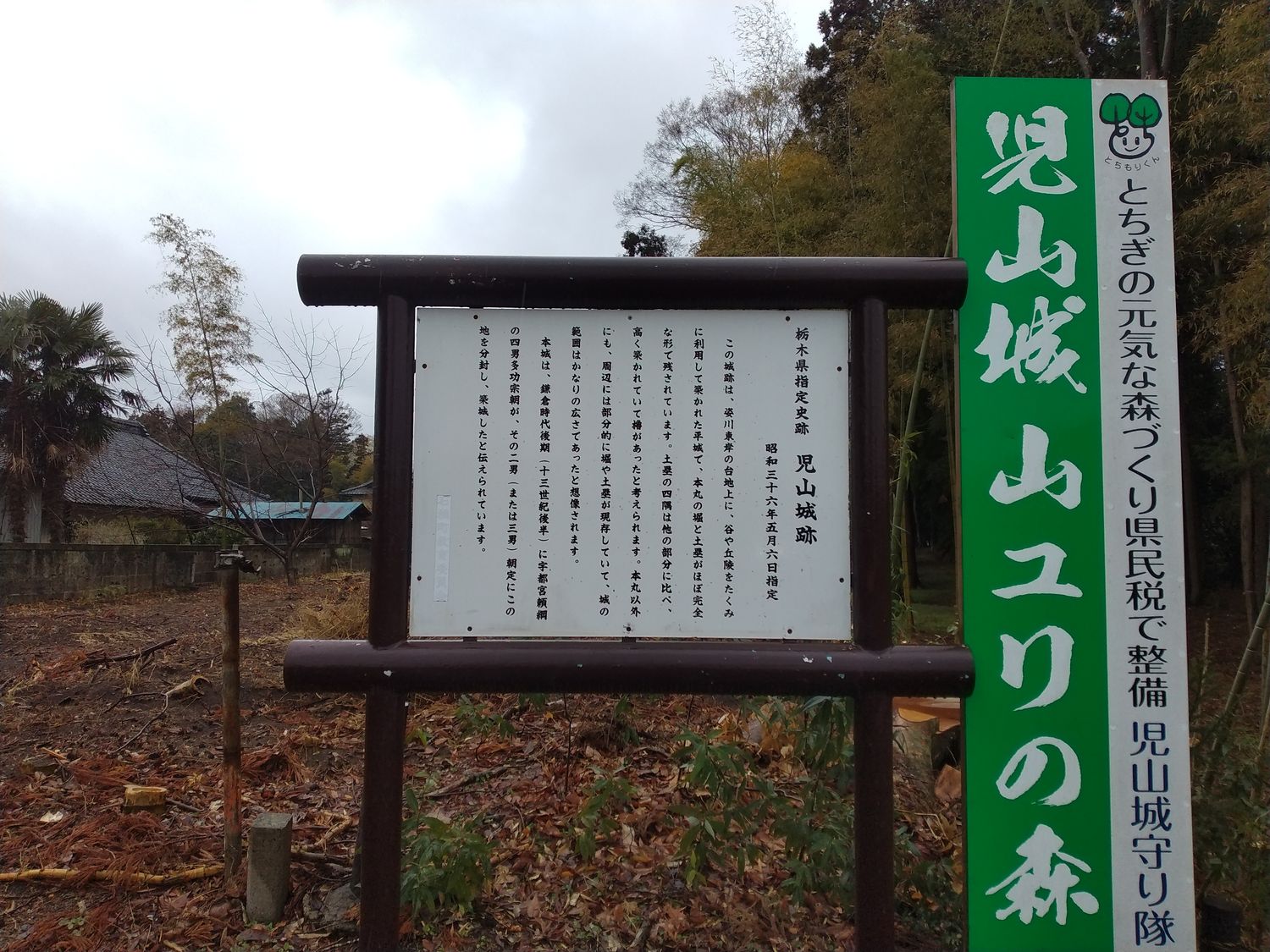 昭和三十六年五月六日指定の、古いほうの案内板。隣に立つ緑の幟には「児山城 山ユリの森」とある。