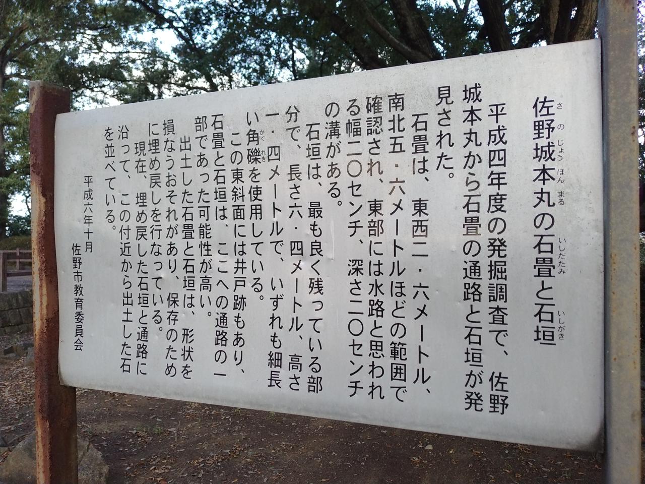 「佐野城本丸の石畳と石垣」の案内板。発掘成果を伝える