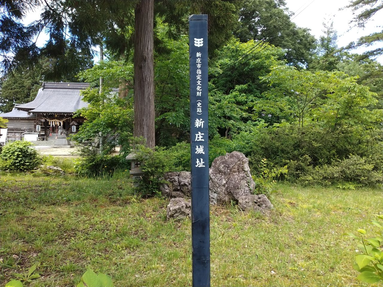 「新庄市指定文化財(史跡)新庄城址」の標柱。奥に見えるのが、本丸跡に鎮座する戸澤神社