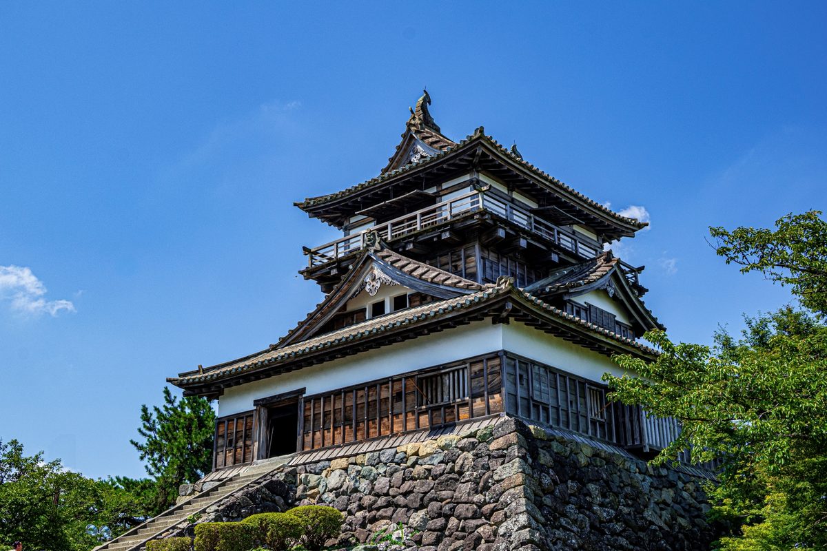 青空の下に立つ丸岡城の現存天守。石瓦の屋根と野面積みの天守台