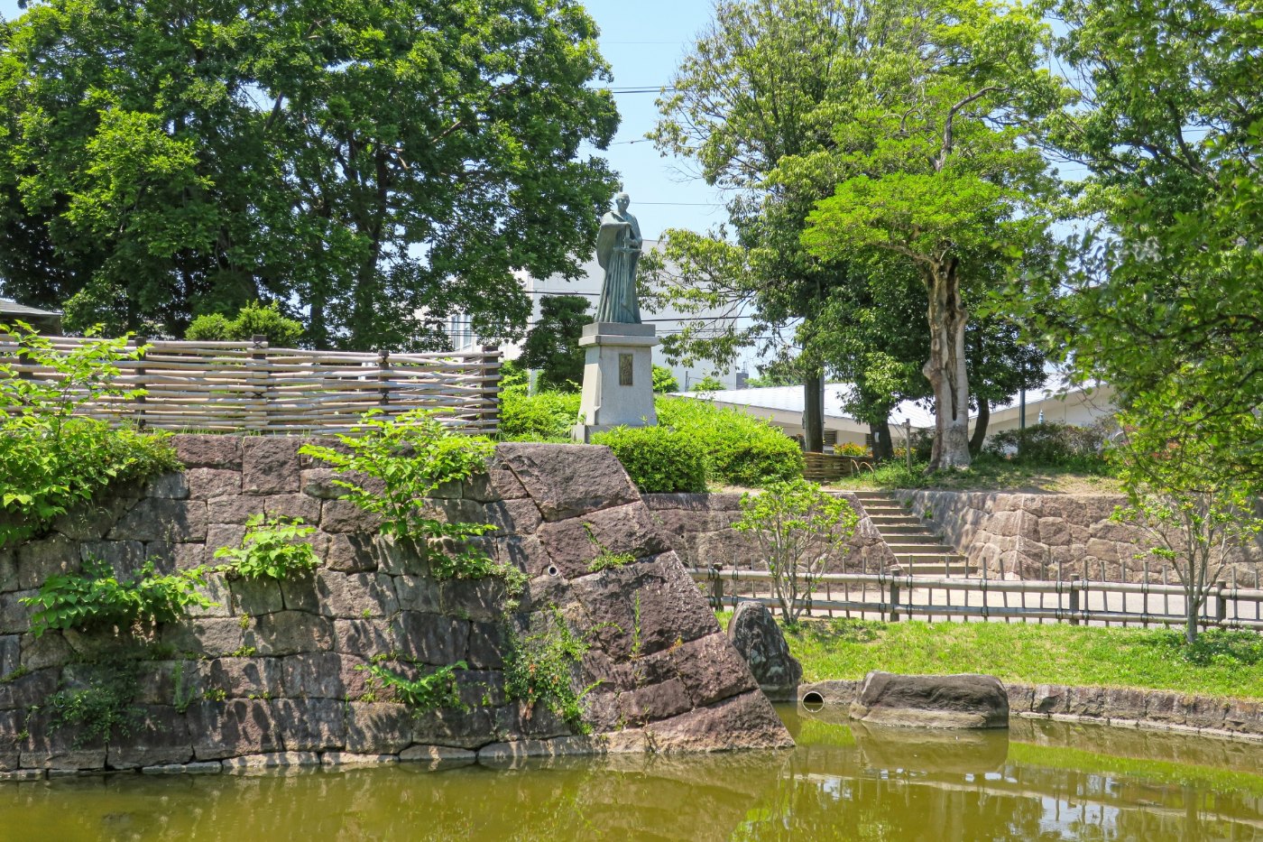 高槻城跡公園の石垣と堀、奥に高山右近の像